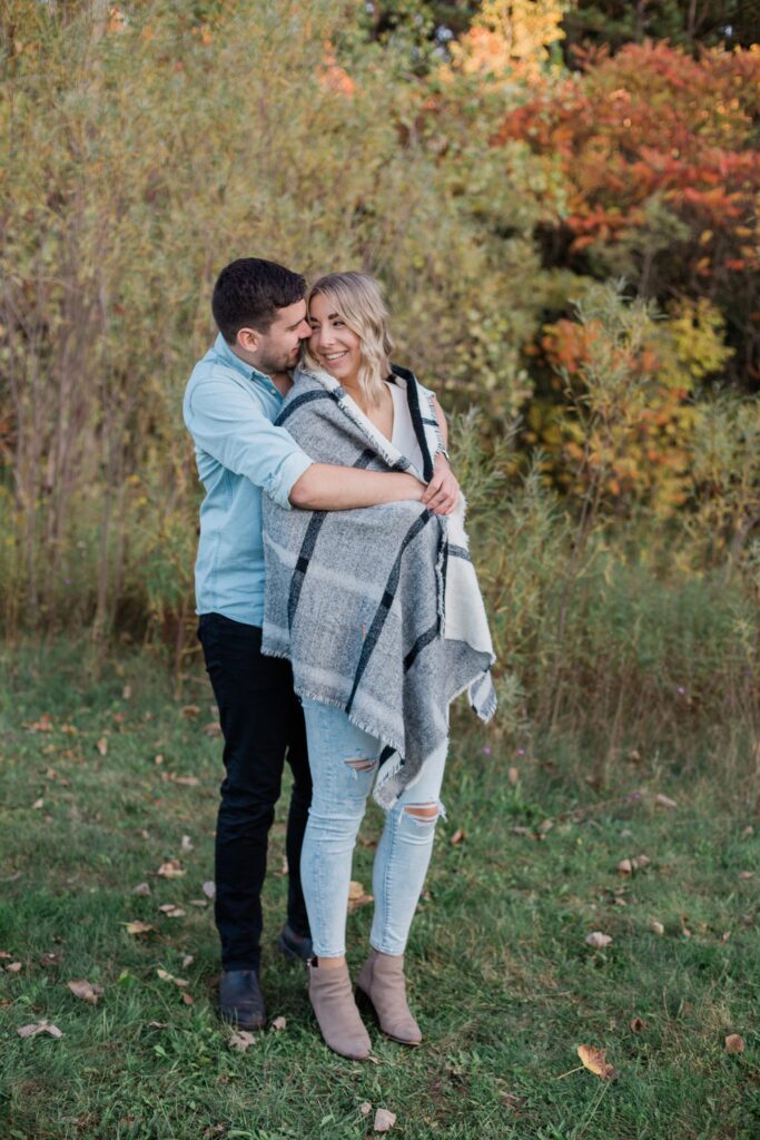 couple snuggled in blanket in field in fall engagement session Huron Natural Area