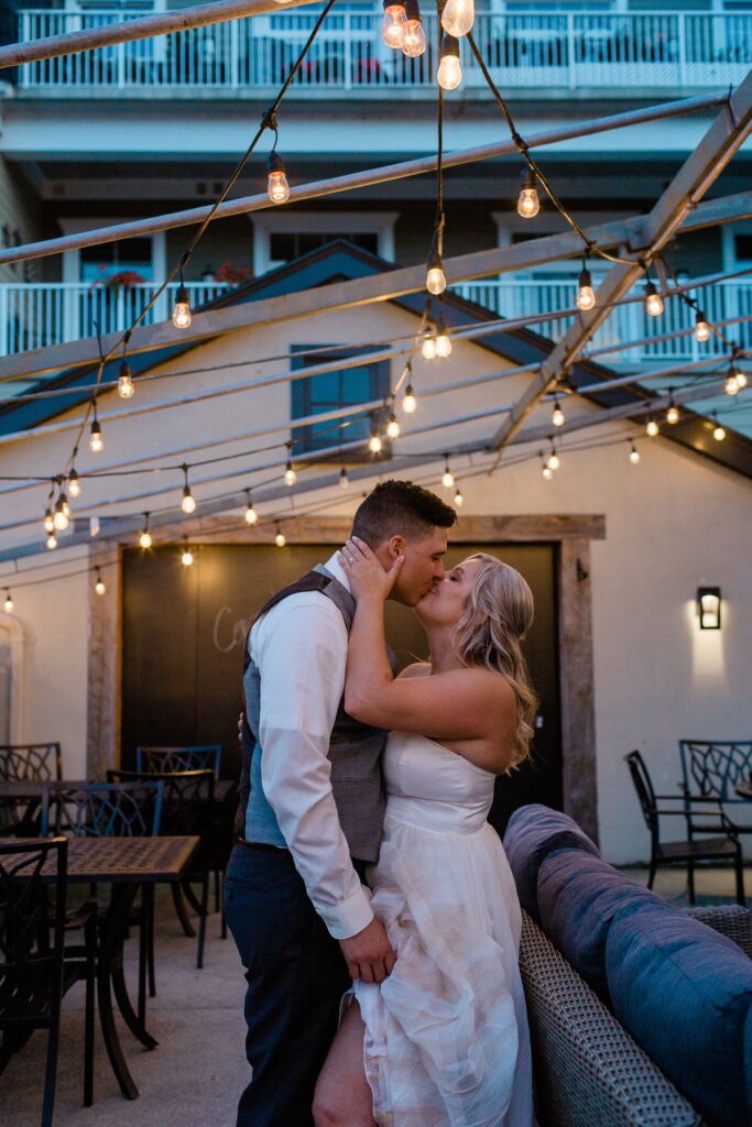 bride and groom kissing at dusk under string lights on intimate patio setting