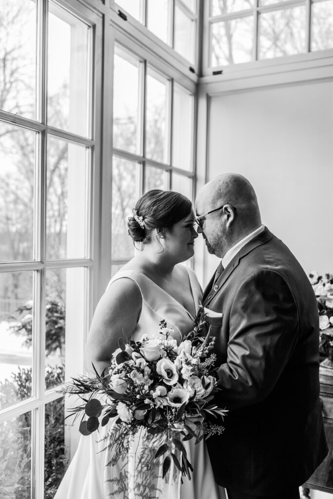 intimate Bride and groom snuggle in conservatory room in black and white