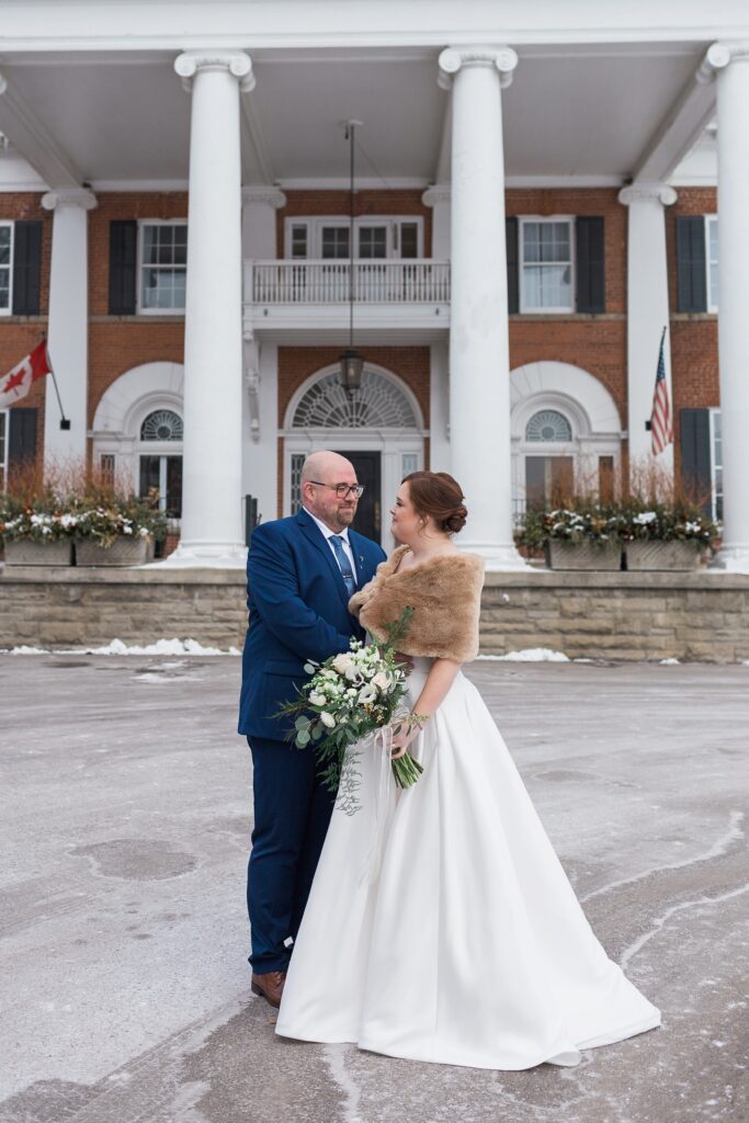 full body photo of bride and groom looking at each other in front of venue