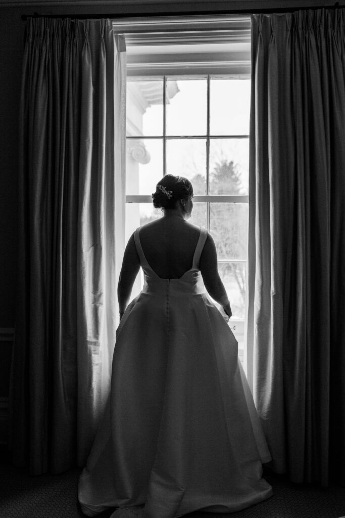full bridal portrait in black and white silhouette of bride looking out window