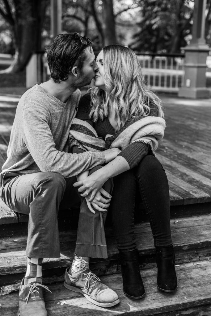 black and white photo of couple sitting in gazebo at Kitchener park kissing