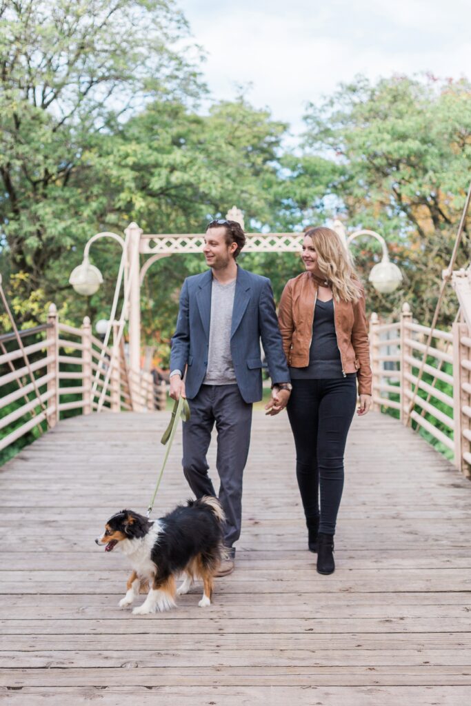 couple holding hands walking dog over bridge at Victoria Park in Kitchener