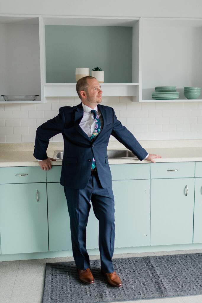 Groom in suit in Kitchen leaning on counter