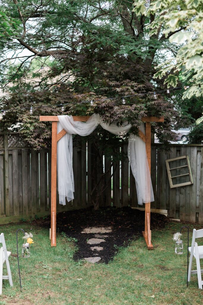 A simple wooden structure with white material for backyard wedding ceremony