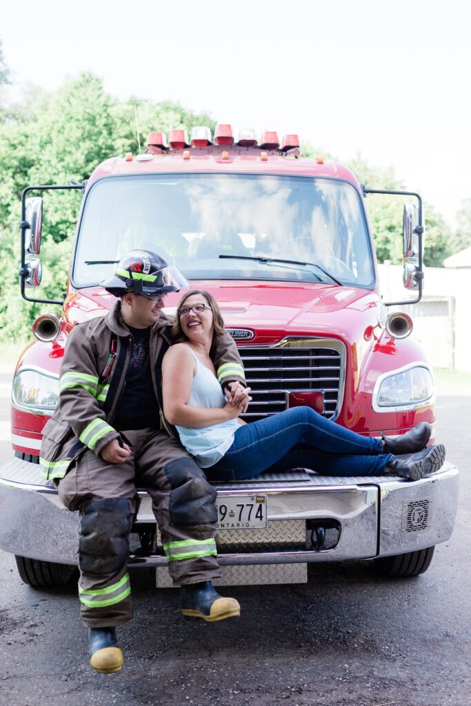 Couple sitting on the front of a fire truck. 