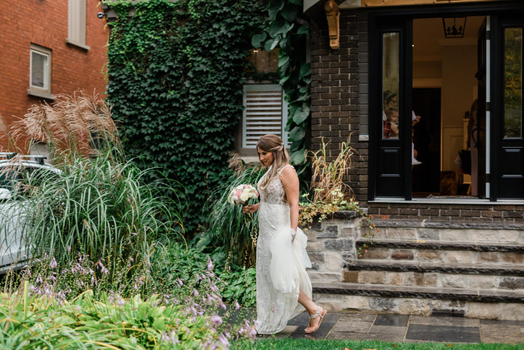 bride walking out of house on wedding day in bridal gown carrying bouquet of flowers