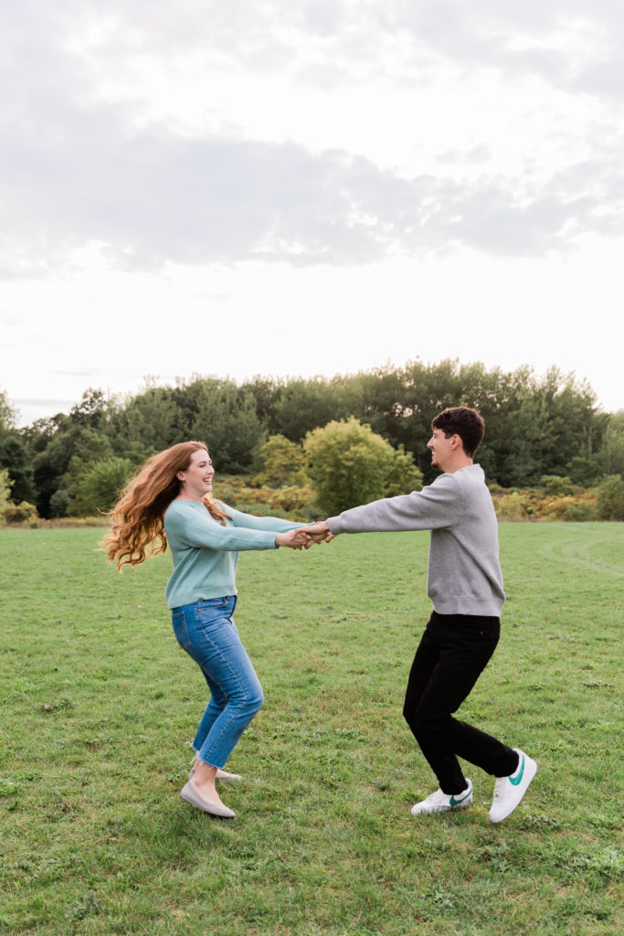 engagement session at Huron Natural Area with couple holding hands spinning in a circle laughing