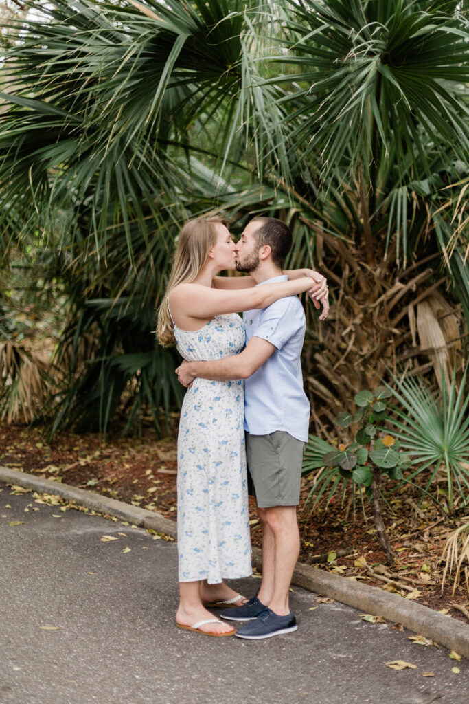 Couple kissing in front of palm tree during their engagement session