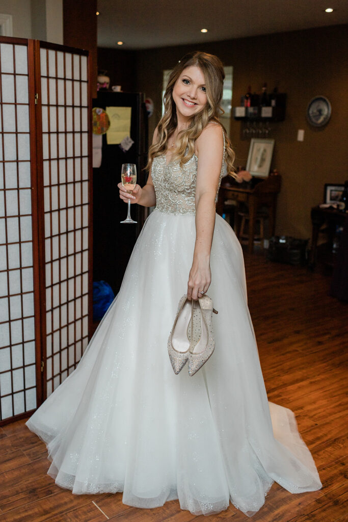 bride on her rainy wedding day holding a glass of champagne and her bridal shoes