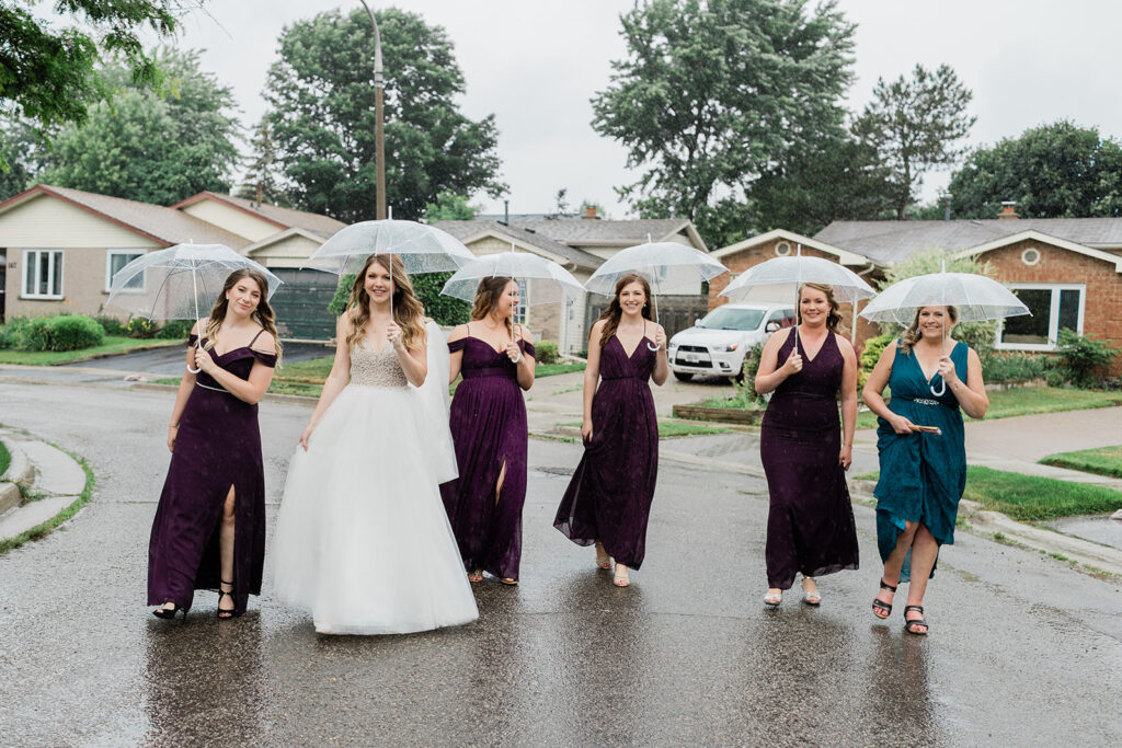 bride and her bridesmaids walking down a city street on a rainy wedding day holding umbrellas