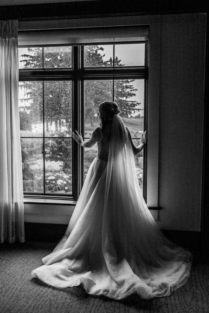 black and white image of a bride looking out the window with her silhouette in the window at Whistle Bear Golf Club on her rainy wedding day