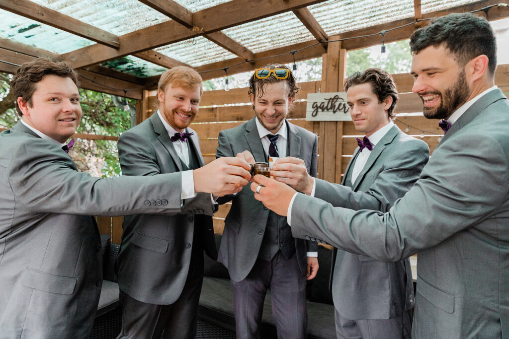 groom and his groomsmen in grey suits holding shot glasses for a cheers