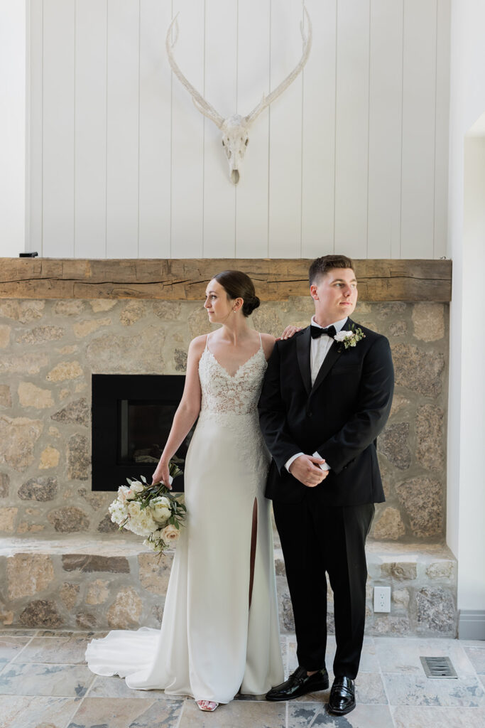 bride and groom in front of fireplace with brides hand on grooms shoulder