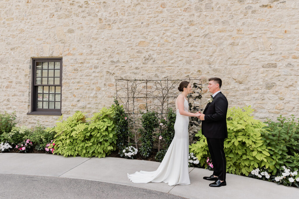 bride and groom holding hands smiling at each other after doing their first look at Elora Mill Hotel and Spa