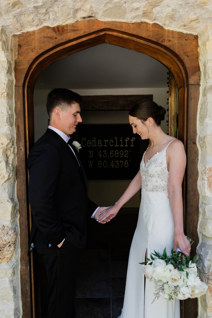 bride and groom standing in doorway at Cedar Cliff holding hands looking down