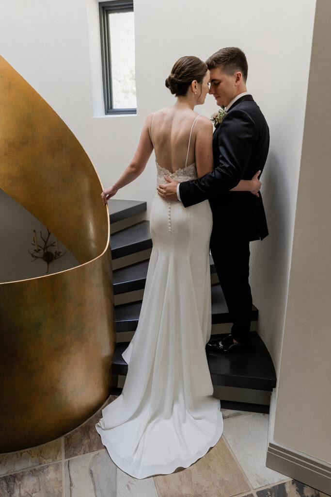 bride and groom standing on spiral staircase snuggled touching noses