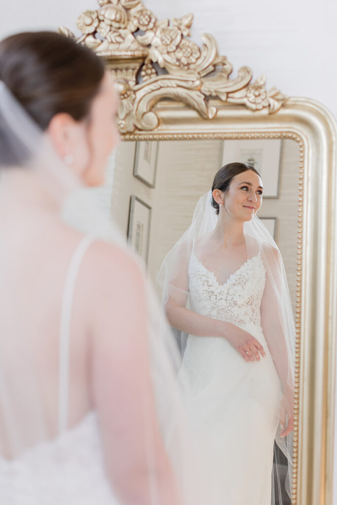bride standing in front of mirror smiling holding veil