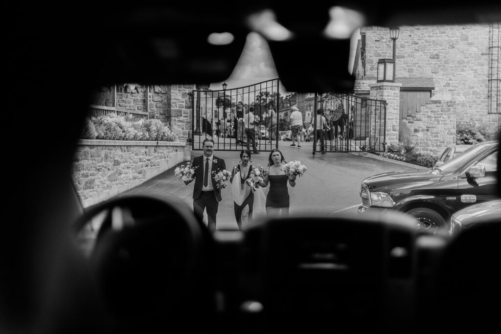 black and white photo from inside limo of wedding party walking carrying flowers